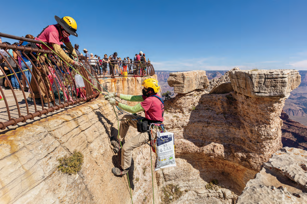 Cliff Littell helps Merlin Repp, a fellow member of the Arizona Mountaineering Club, back up to Mather Point during the 2020 Grand Canyon Over-the-Rim Cleanup. Repp is toting a bag of trash retrieved from the ledges below the overlook, while Littell is untying a bag of coins Repp collected.