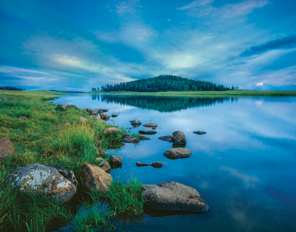 After sunset, the calm water of Crescent Lake, in the White Mountains, reflects the evergreens on a nearby volcanic knoll. Located just north of Big Lake, this reservoir is known for its crystal-clear water and for attracting deer, elk, foxes and other wildlife. | Jack Dykinga | ARCA-SWISS F-FIELD C 4X5, FUJICHROME VELVIA, 5 SEC, F/45, ISO 50, 75 MM LENS