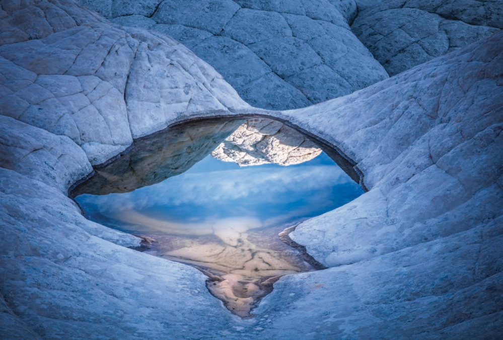 A shallow pool in the textured “brain rock” of White Pocket, in the Vermilion Cliffs of Northern Arizona, mirrors sky and stone in early morning light. A high-clearance, four-wheel-drive vehicle is required to reach this extremely remote site. | Suzanne Mathia | Canon EOS 5DS R, 1/50 SEC, F/11, ISO 100, 70 MM LENS