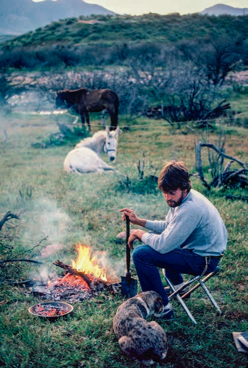 Near Theodore Roosevelt Lake, Troy cooks dinner and relaxes with the mules and Little Boogie, a cattle dog who joined them during the hike. Of note, this fire does not conform to Leave No Trace principles, which hadn’t been established yet — fires like this were typical back then.
