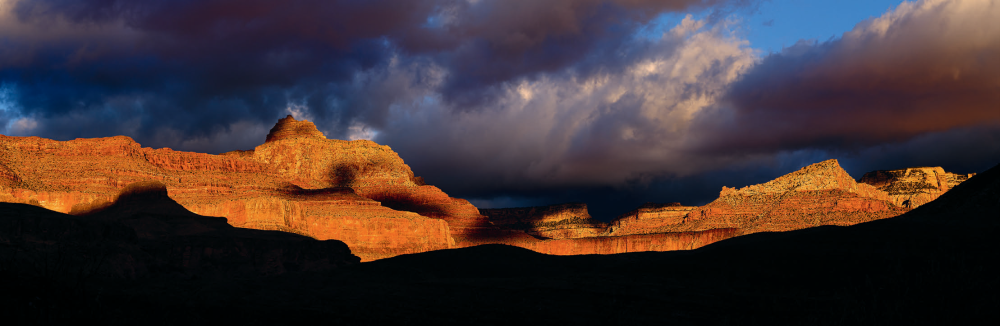 Storm clouds move across Vishnu Temple and the North Rim as the day’s first rays of light paint the cliffs in fiery hues. | ADAM SCHALLAU