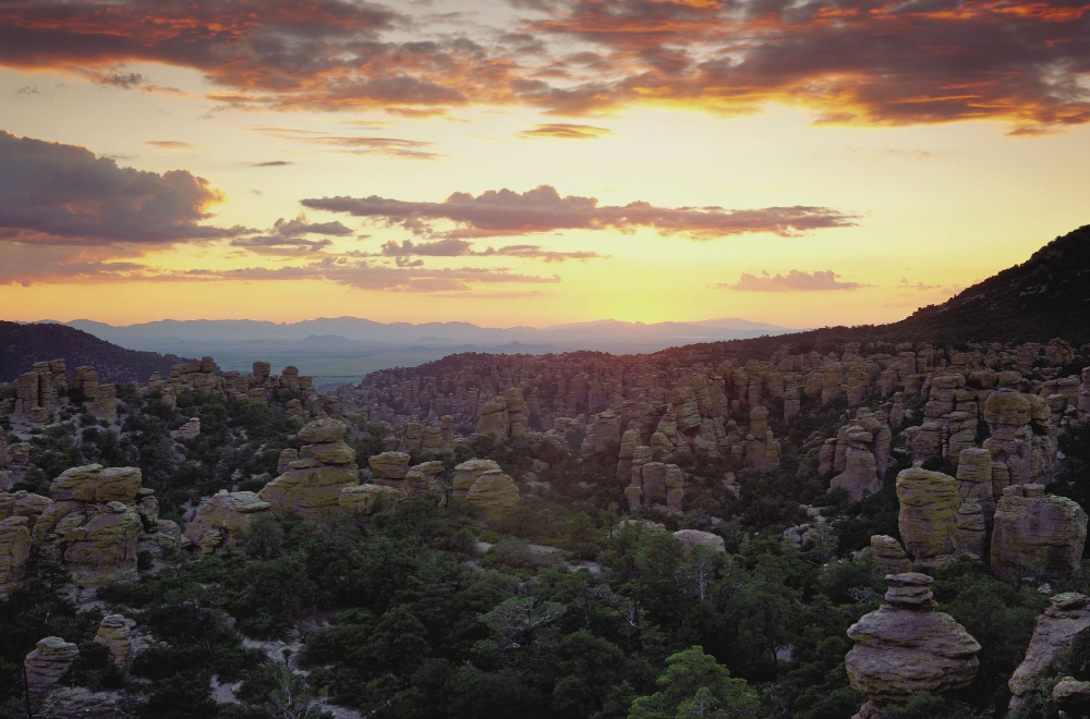 In a western view from Massai Point, a brilliant sunset warms Chiricahua National Monument's Wonderland of Rocks. The vista beyond comprises Sulphur Springs Valley and the Dragoon Mountains.