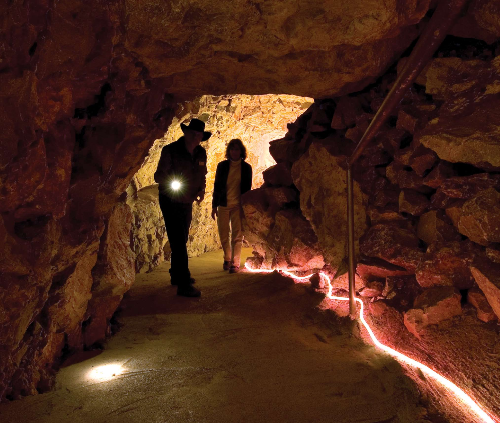 Immersed in the red glow of artificial light, Jerry Keeler and Susan Hamilton head toward the Chapel of Ages, one of the giant underground spaces in Grand Canyon Caverns that stored enough food and water to support 2,000 people for two weeks during the Cuban Missile Crisis.