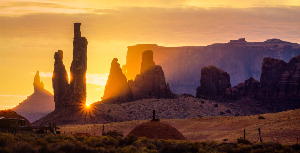 The sun peeks between the iconic spires of Monument Valley Navajo Tribal Park.