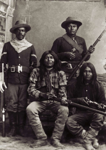 An unidentified black "Buffalo Soldier" poses with three unnamed Apache scouts, on the sharp edge of the bitter contradictions that attended the Indian Wars in the United States.