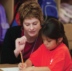Vicki Wilson's weeklong stint as a tutor at the Tuba City Boarding School on the Navajo Indian Reservation is one example of a sustainable community project building bridges of friendship through Amizade volunteers. Midway through her week, Wilson guides kindergartner Gerolle Butler through a writing exercise.